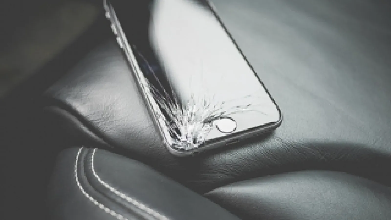 Cell phone with crack in screen on car seat in sepia